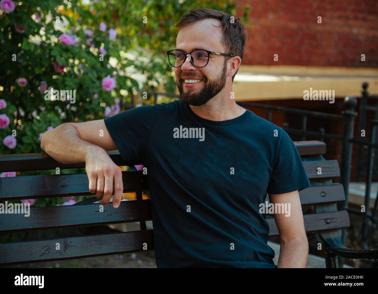 Man in black t-shirt, beard an glasses on the bench in summer city Stock Photo