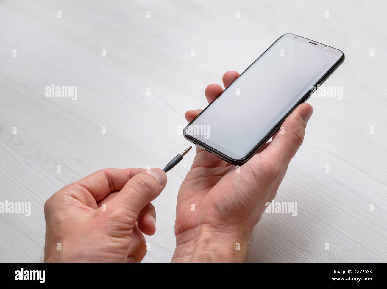 Connecting audio jack on a mobile phone. 3.5 mm audio jack and mobile phone in hands. Stock Photo