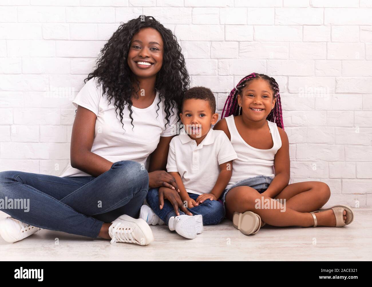 Black millennial mom sitting on floor with daughter and son Stock Photo