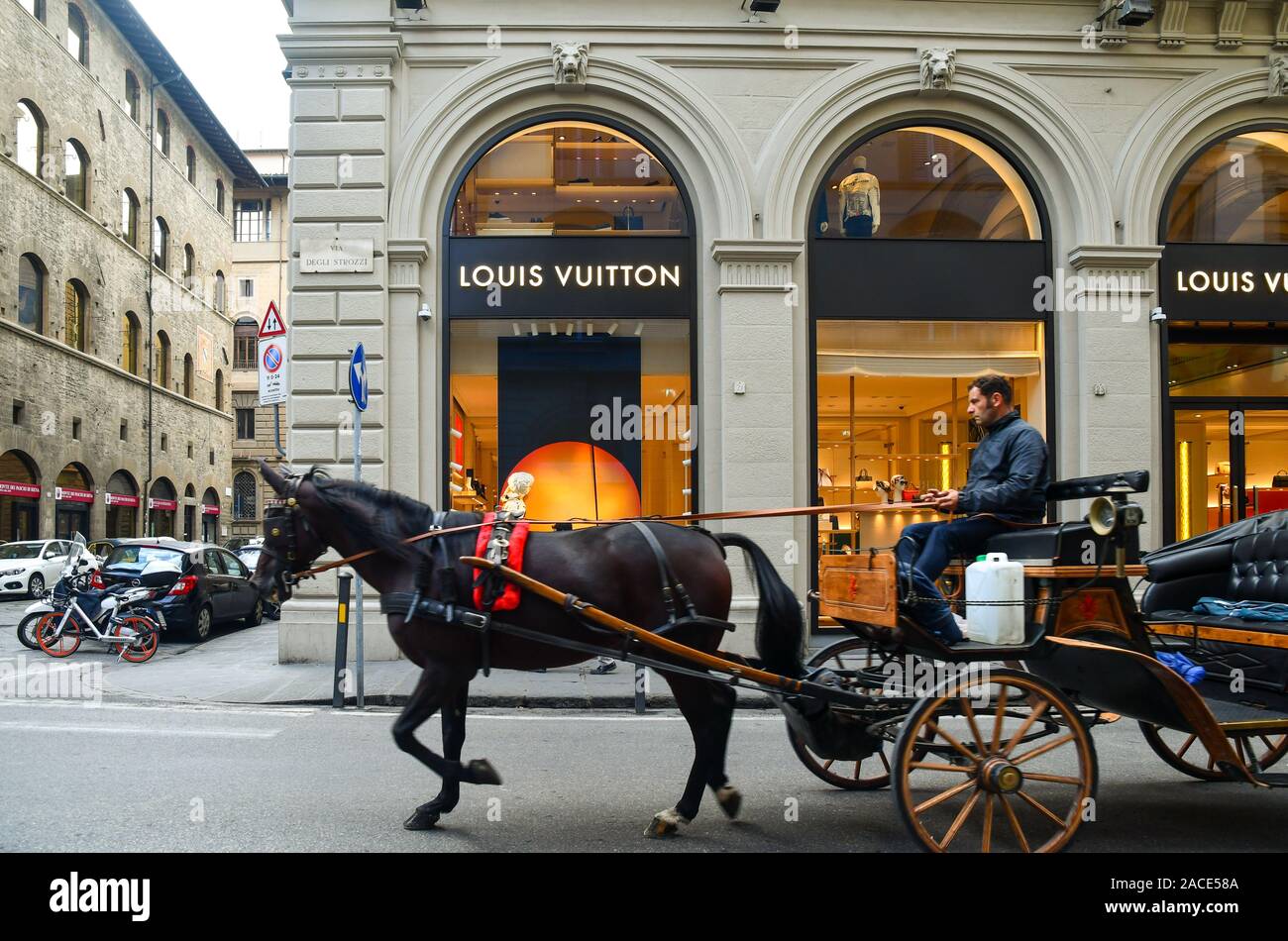 Horse-drawn carriage passing in front of the Louis Vuitton boutique, famous high-fashion house, in the historic centre of Florence, Tuscany, Italy Stock Photo