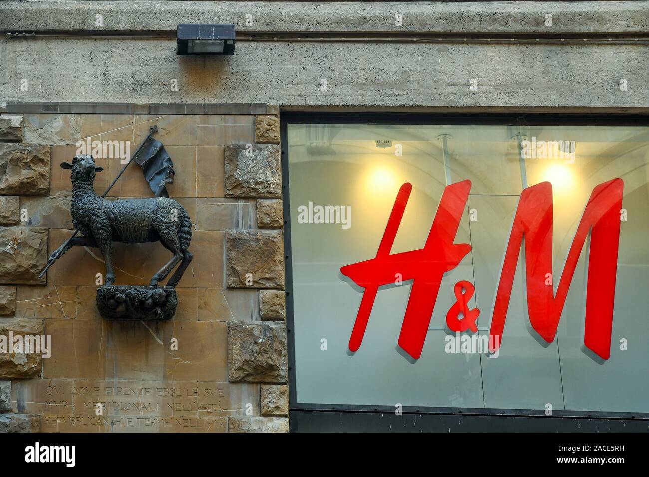 Detail of Palazzo della Borsa Merci with the bronze lamb, symbol of  Arte della Lana, next to the shop sign of H&M department store, Florence, Italy Stock Photo