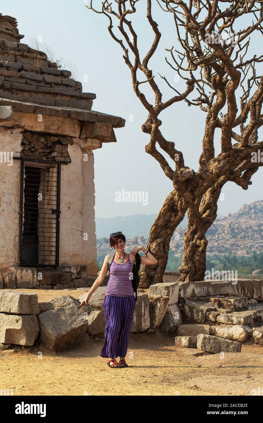 Tourist girl near an ancient building with a tree. The Group of Monuments at Hampi was the centre of the Hindu Vijayanagara Empire in Karnataka state Stock Photo