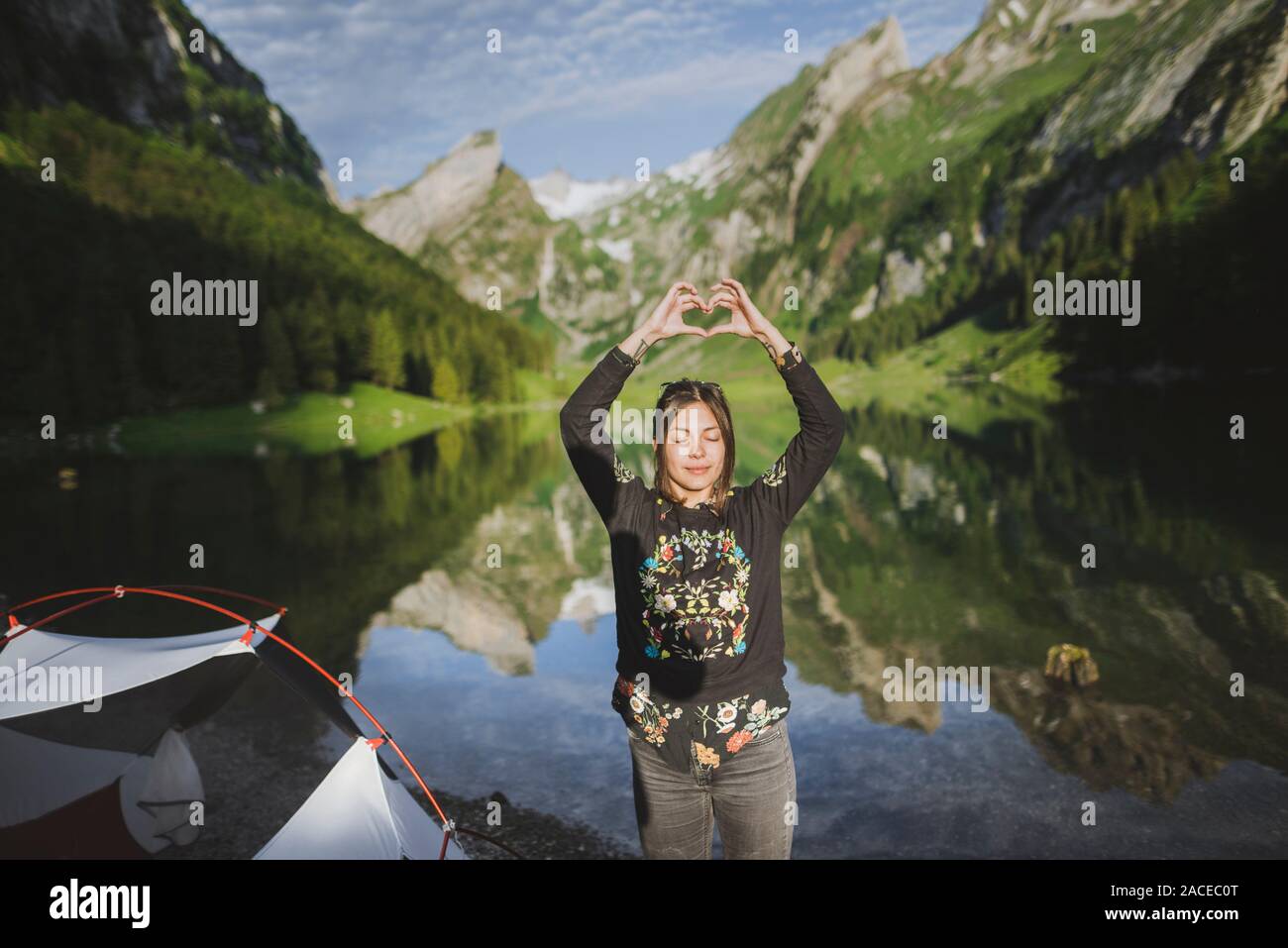 Woman making heart hand sign by Seealpsee lake in Appenzell Alps, Switzerland Stock Photo