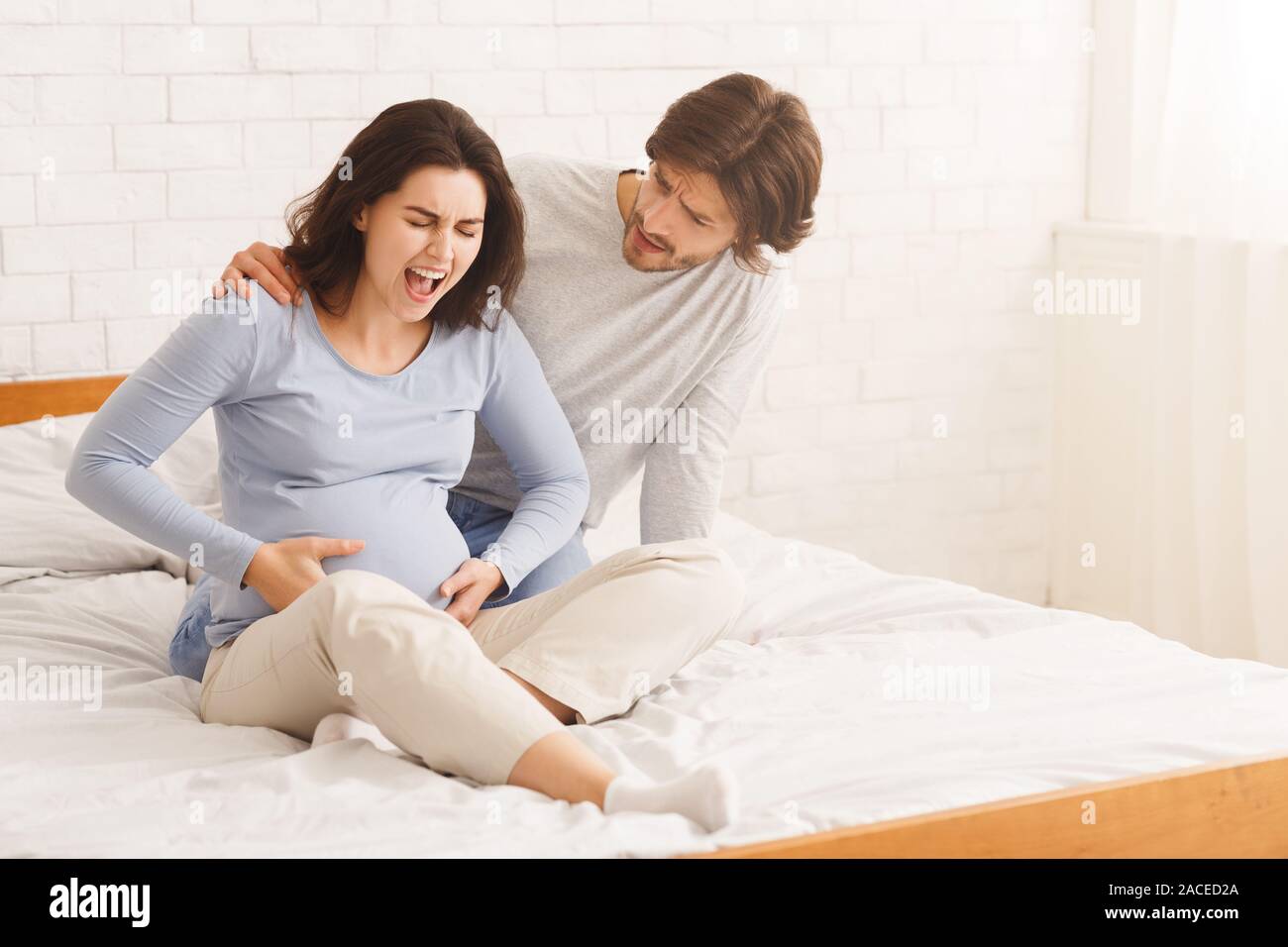 Worried husband comforting pregnant wife that suffering from prenatal contractions Stock Photo