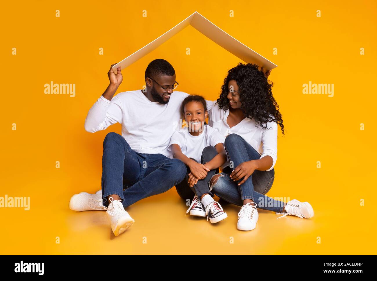 Adoptive parents holding carton roof above little black girl Stock Photo