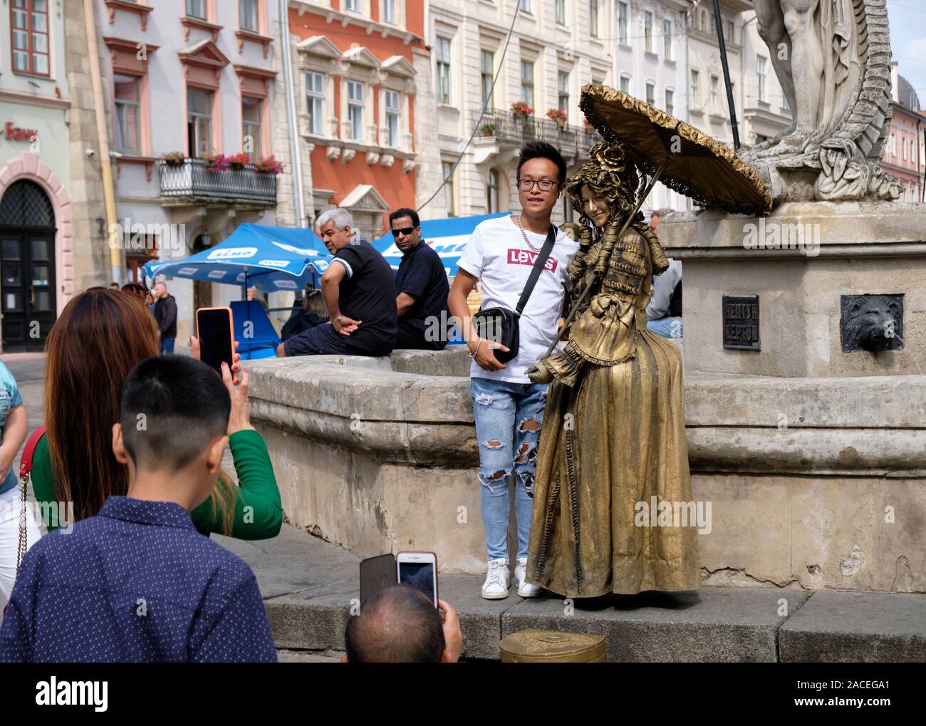 Tourist posing with living "bronzed" statue performer women dress in medieval outfit.  Lviv, Ukraine Stock Photo