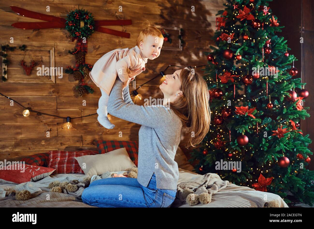 Young mother playing with baby near Christmas tree Stock Photo