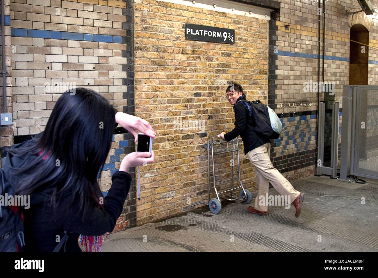 Tourist posing at Harry Potter's platform 9 3/4 at King’s Cross Station Stock Photo