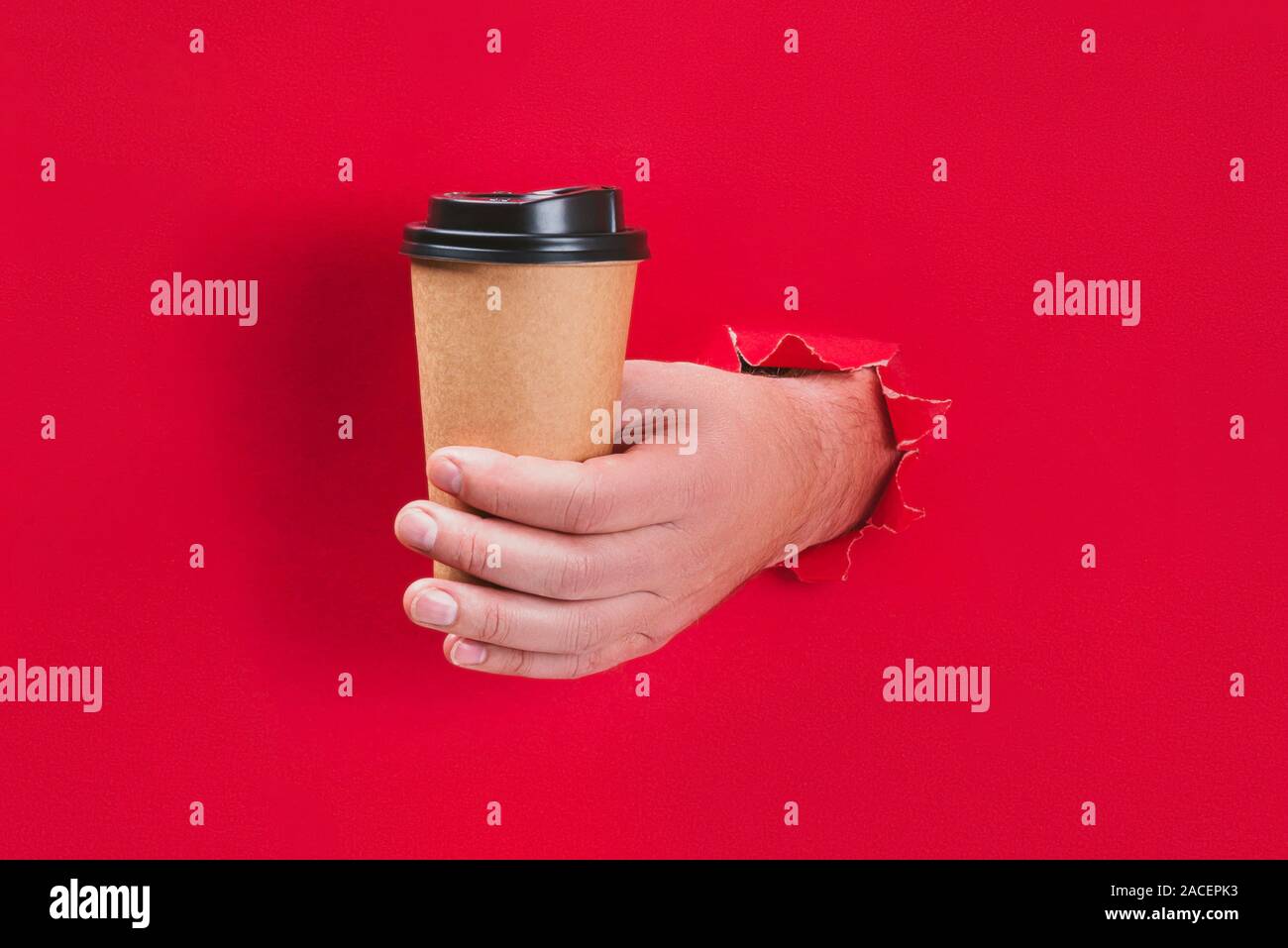 Male hand holding craft paper coffee cup through a hole in red ...