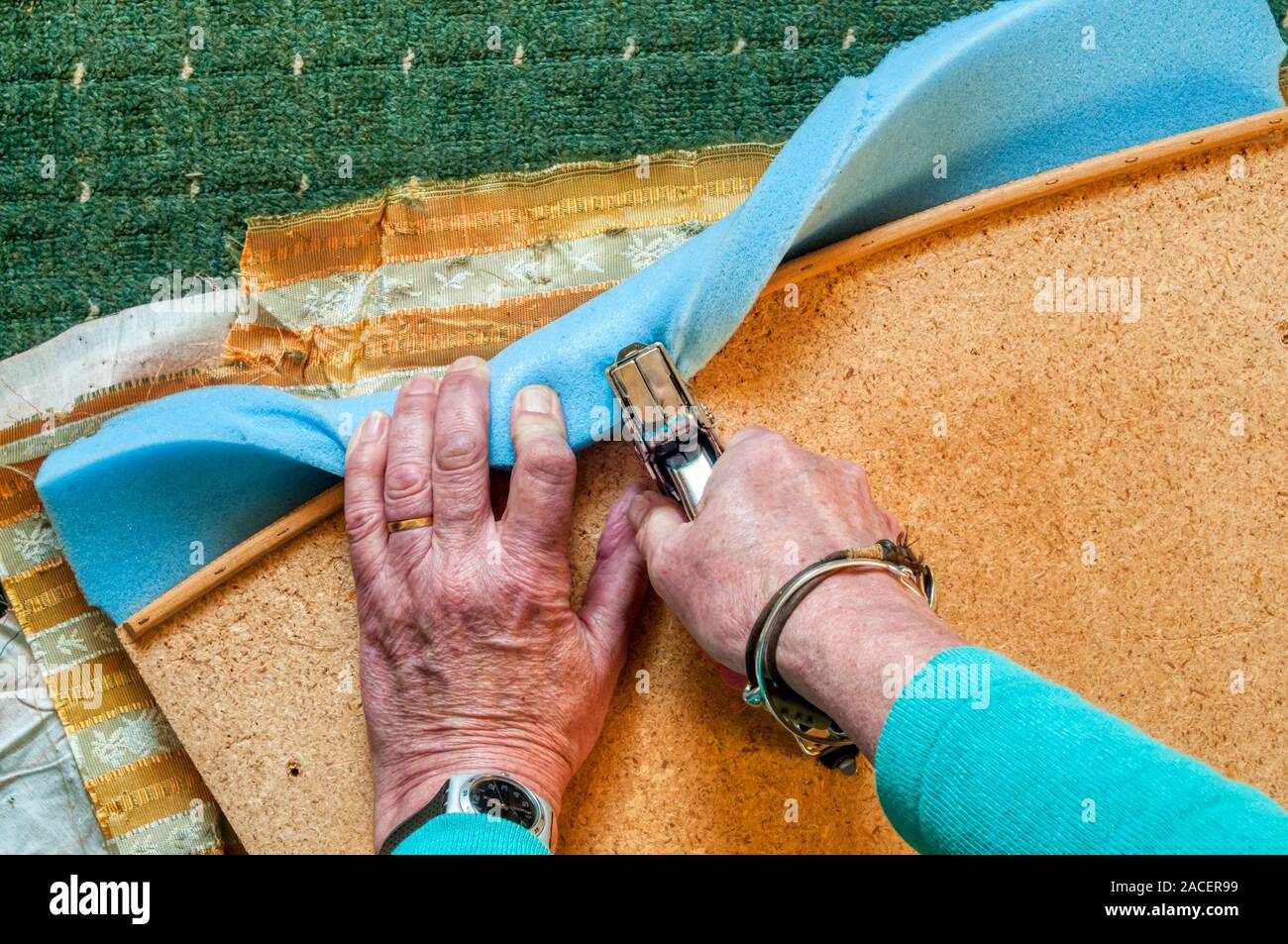 3 of 4 - Recovering an old dining chair - pulling new foam padding round and stapling to underside of seat. Search UIDIY2 for sequence. Stock Photo