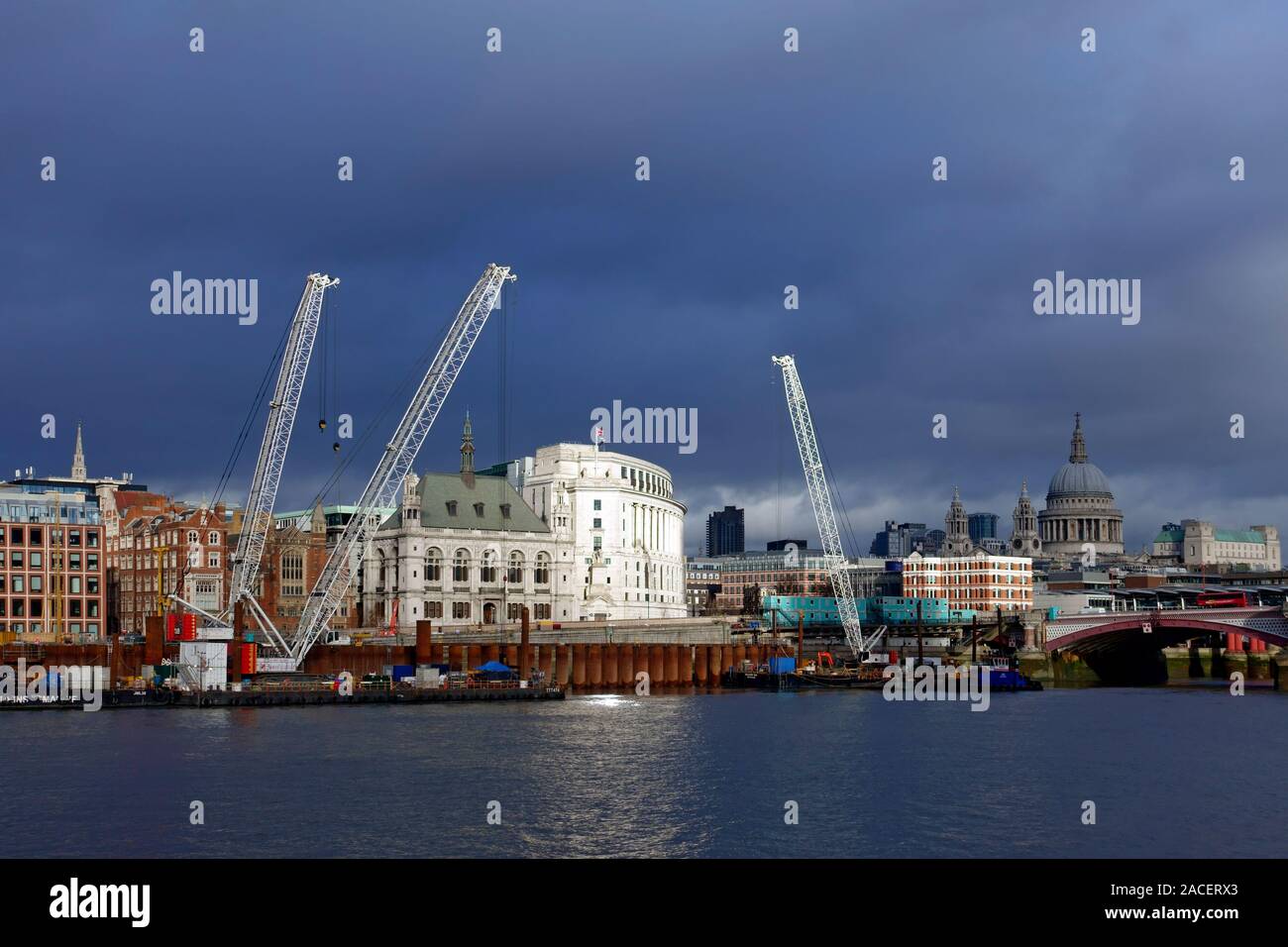 Dark skies over the Blackfriars district of London with large cranes on the waterfront and Greyfriars Bridge to the right Stock Photo