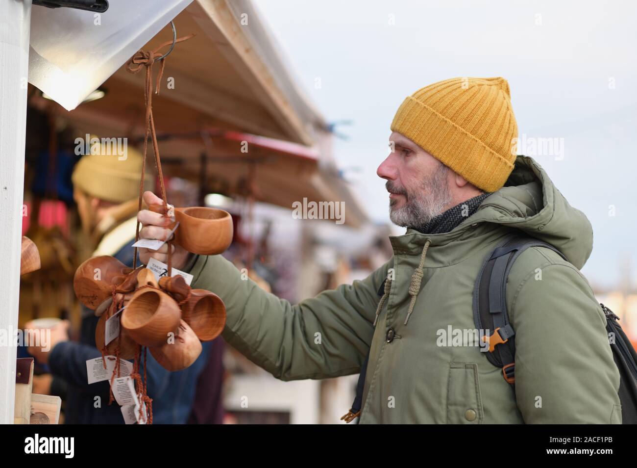 Mature bearded man with backpack selecting the kuksa, Finnish traditional wooden cup, on the Christmas market on Kauppatori square in Helsinki, Finlan Stock Photo