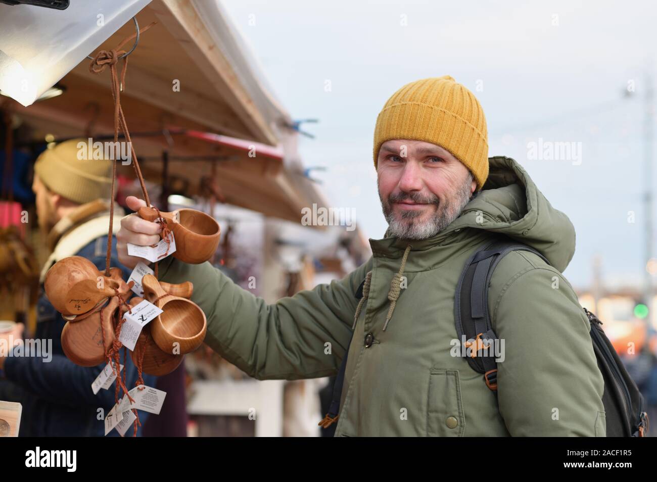 Mature bearded man with backpack selecting the kuksa, Finnish traditional wooden cup, on the Christmas market on Kauppatori square in Helsinki, Finlan Stock Photo