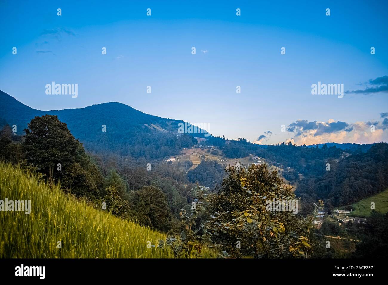 paisaje hermoso de atardecer con bosques y siembras de trigo y montañas de cajola Quetzaltenango, casas de personas en el valle Stock Photo