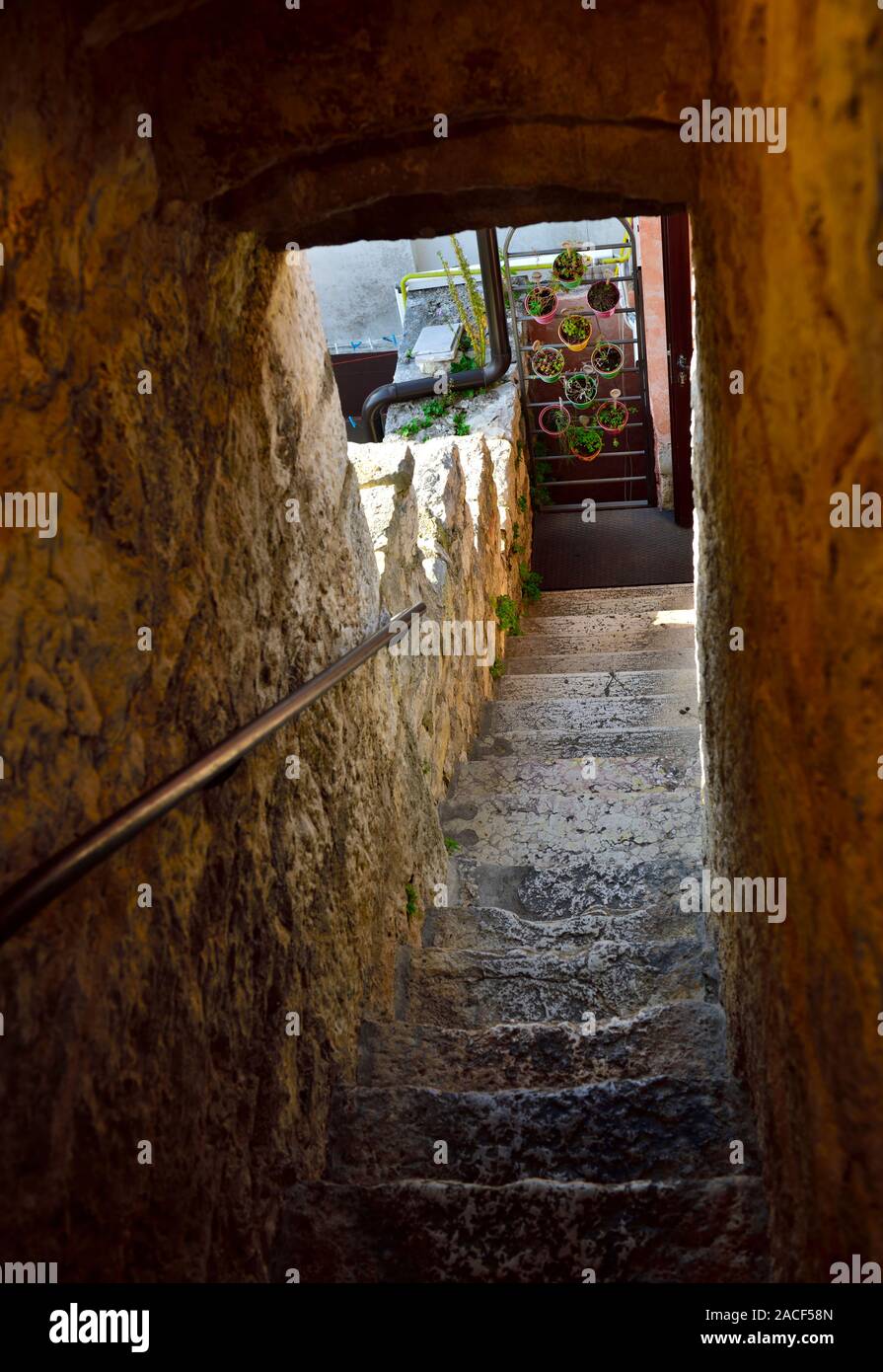Looking down through narrow tunnel with old worn steps to flowerpots Stock Photo