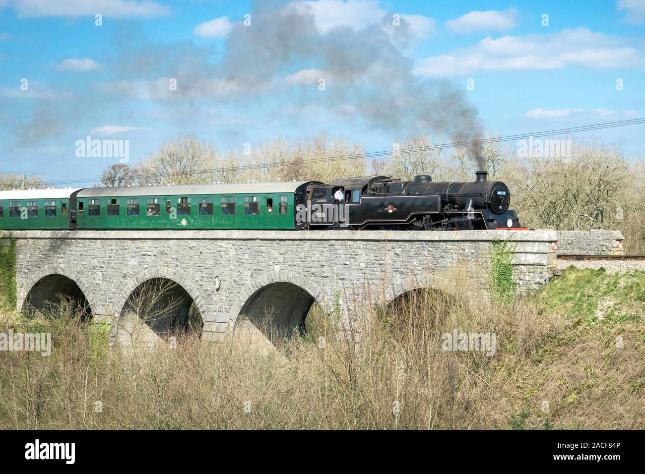 Black railway and green coach pass the Corfe bridge, Dorset, UK Stock Photo