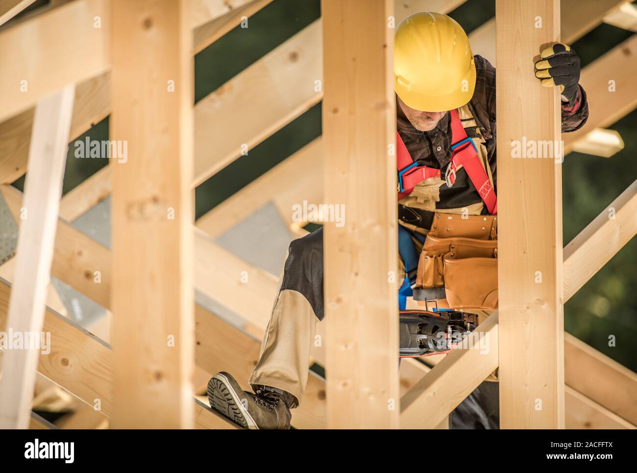 Construction Contractor Worker in His 30s Wearing Hard Hat and the Wooden House Frame. Stock Photo
