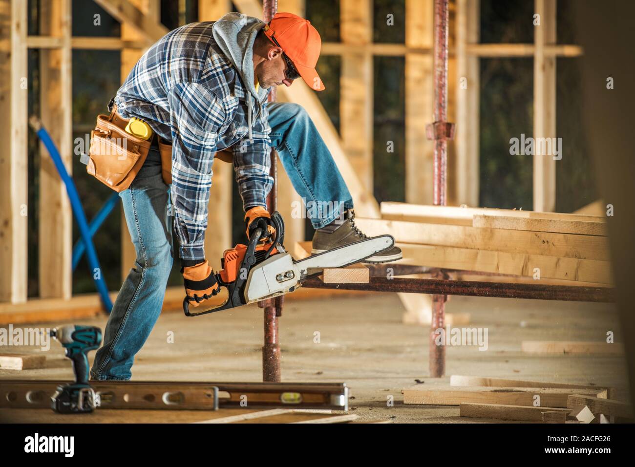 Caucasian Contractor Worker with Gasoline Chainsaw Cutting Wood Beams. Wooden Frame House Construction. Stock Photo