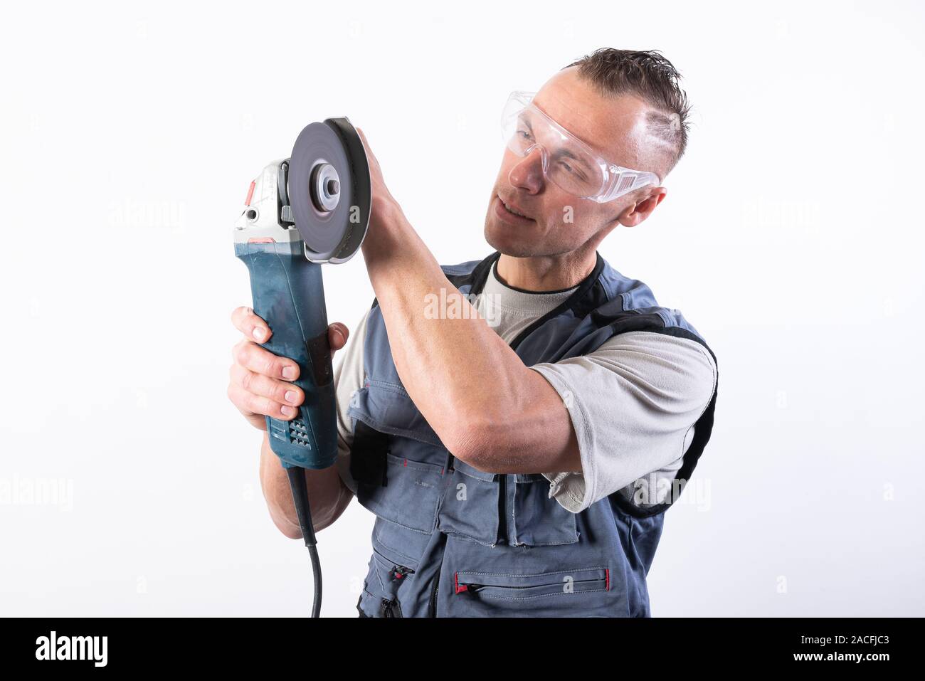 The builder in goggles, with an angle grinder in his hands. Stock Photo