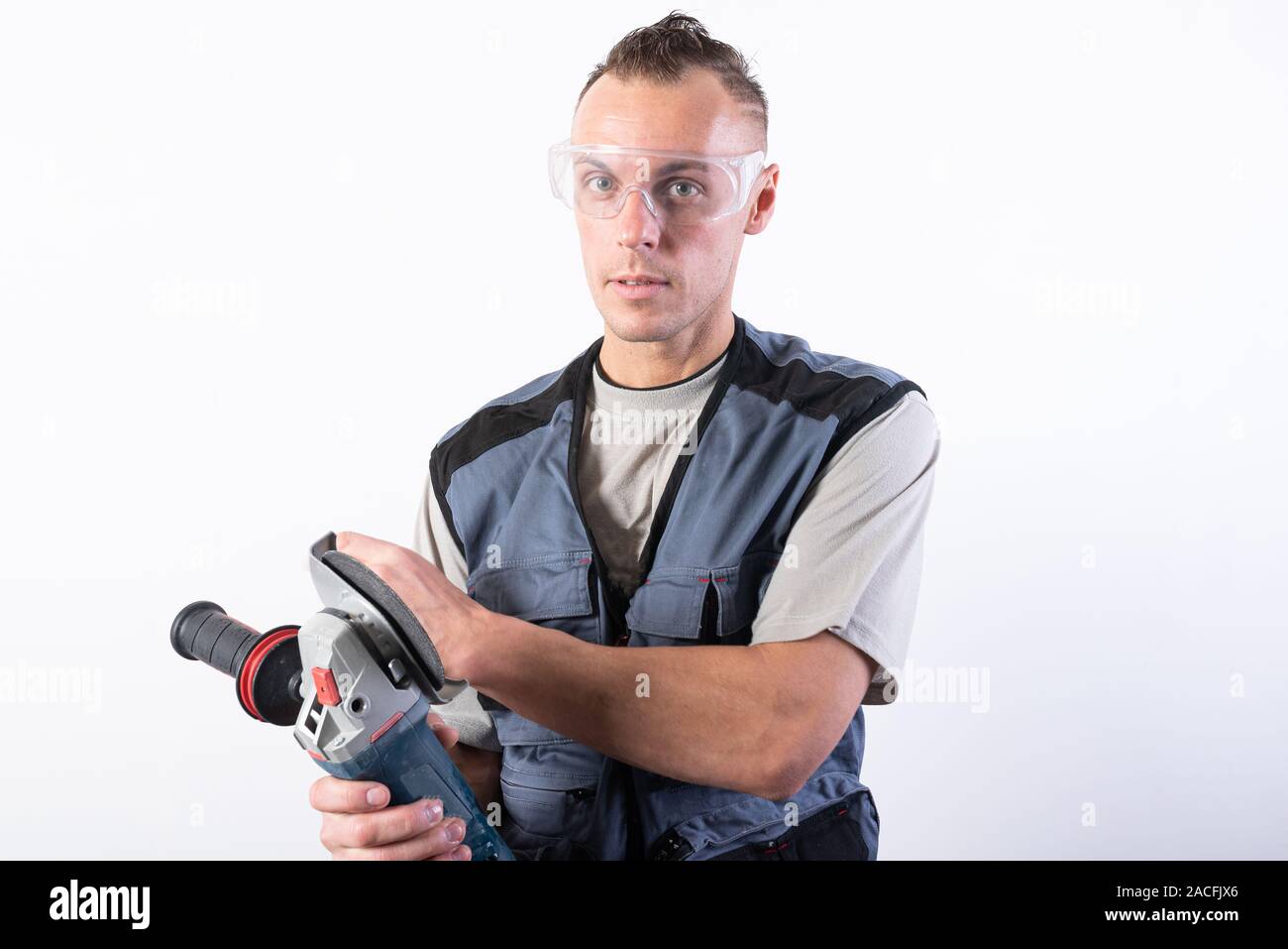 The builder in goggles, with an angle grinder in his hands. Stock Photo