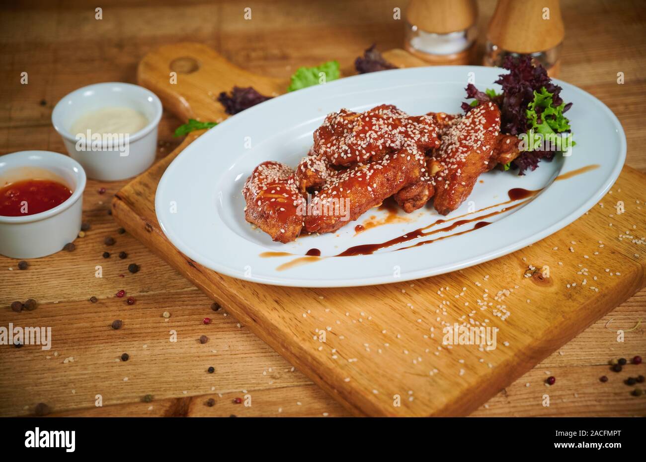 Serving of delicious spicy chicken wings with sesame seeds and sweet chili sauce on white wooden board Stock Photo