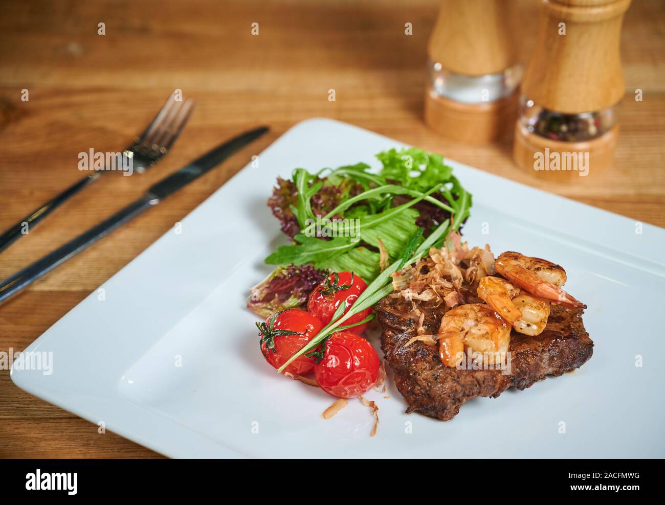 Grilling steak. Dish of meat on a plate adding with shrimp, tomatoes and salad. Arrangement with cutlery Stock Photo