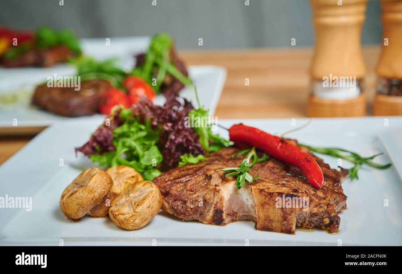 Grilling steak. Dish of meat on a plate adding with mushrooms, salad and red pepper Stock Photo