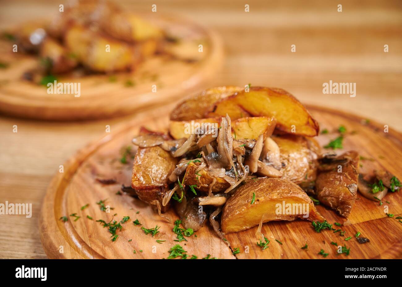 Wooden board with tasty potato wedges with mushrooms on table. Roasted potatoes with mushrooms Stock Photo
