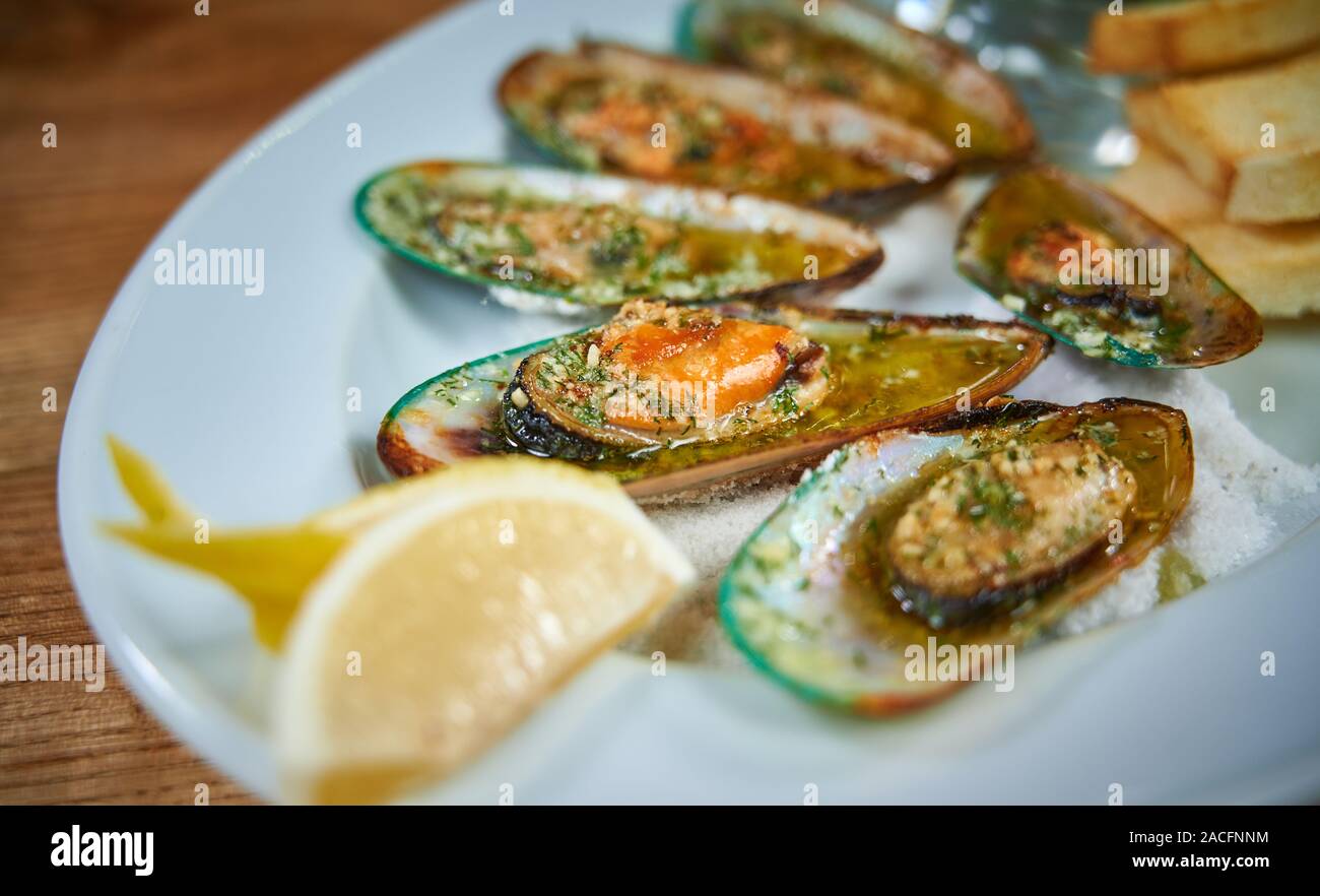 Mussels with garlic sauce serving on white plate in restaurant, close up Stock Photo