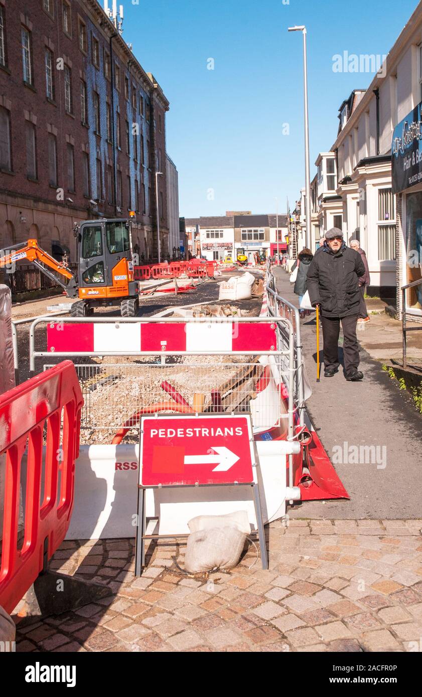 Road works constructing a new road layout. Safety barriers and temporary pedestrian footpath in position. Man with stick walking along footway. Stock Photo