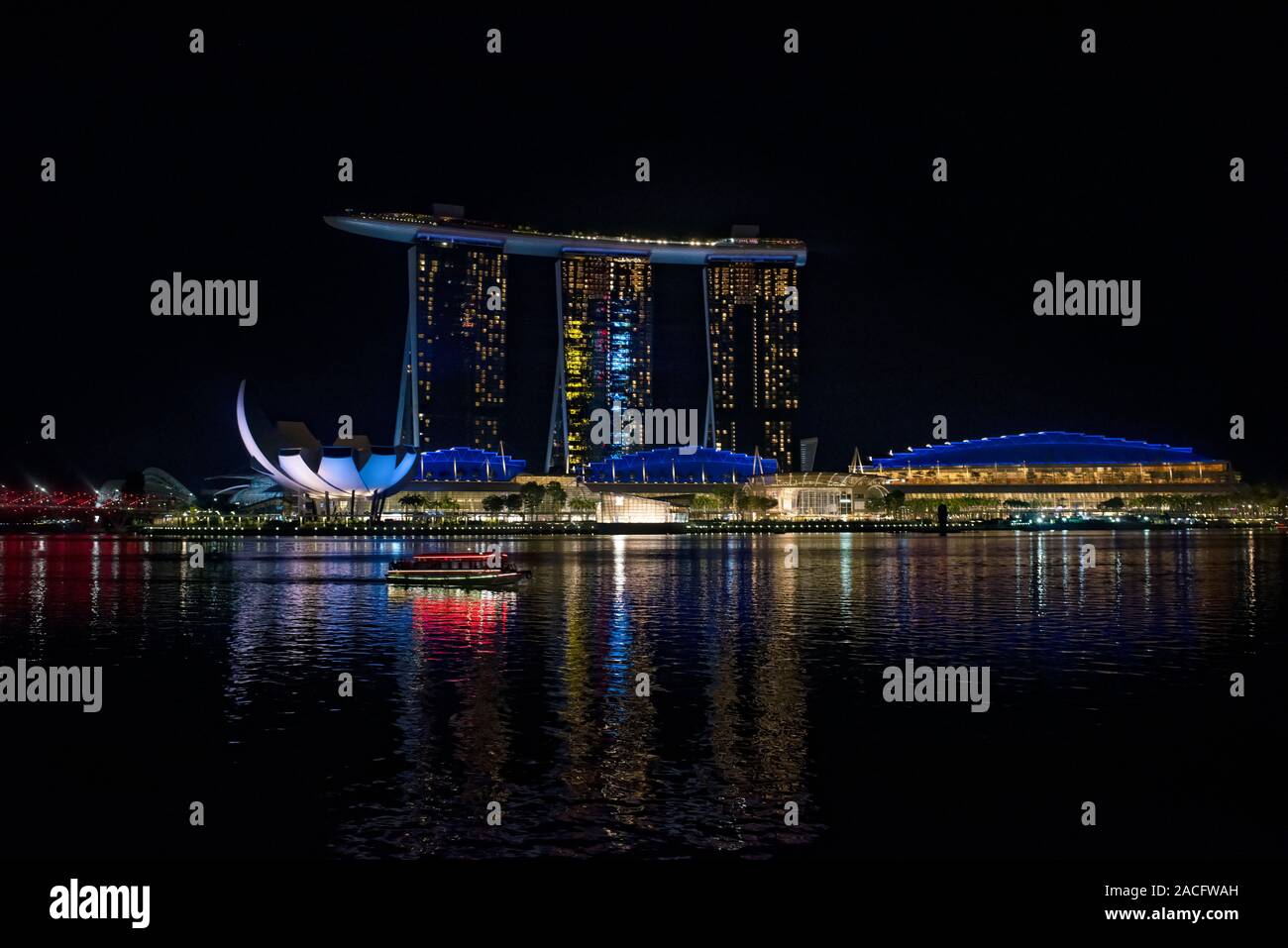 The lights of Marina Bay Sands hotel reflecting on the water of Marina Ba with a tourist sightseeing boat, Singapore Stock Photo