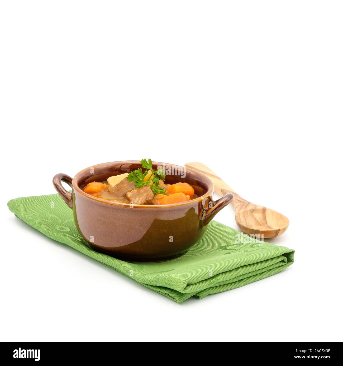 Bowl of hearty beef stew on a green napkin on a white background. Stock Photo