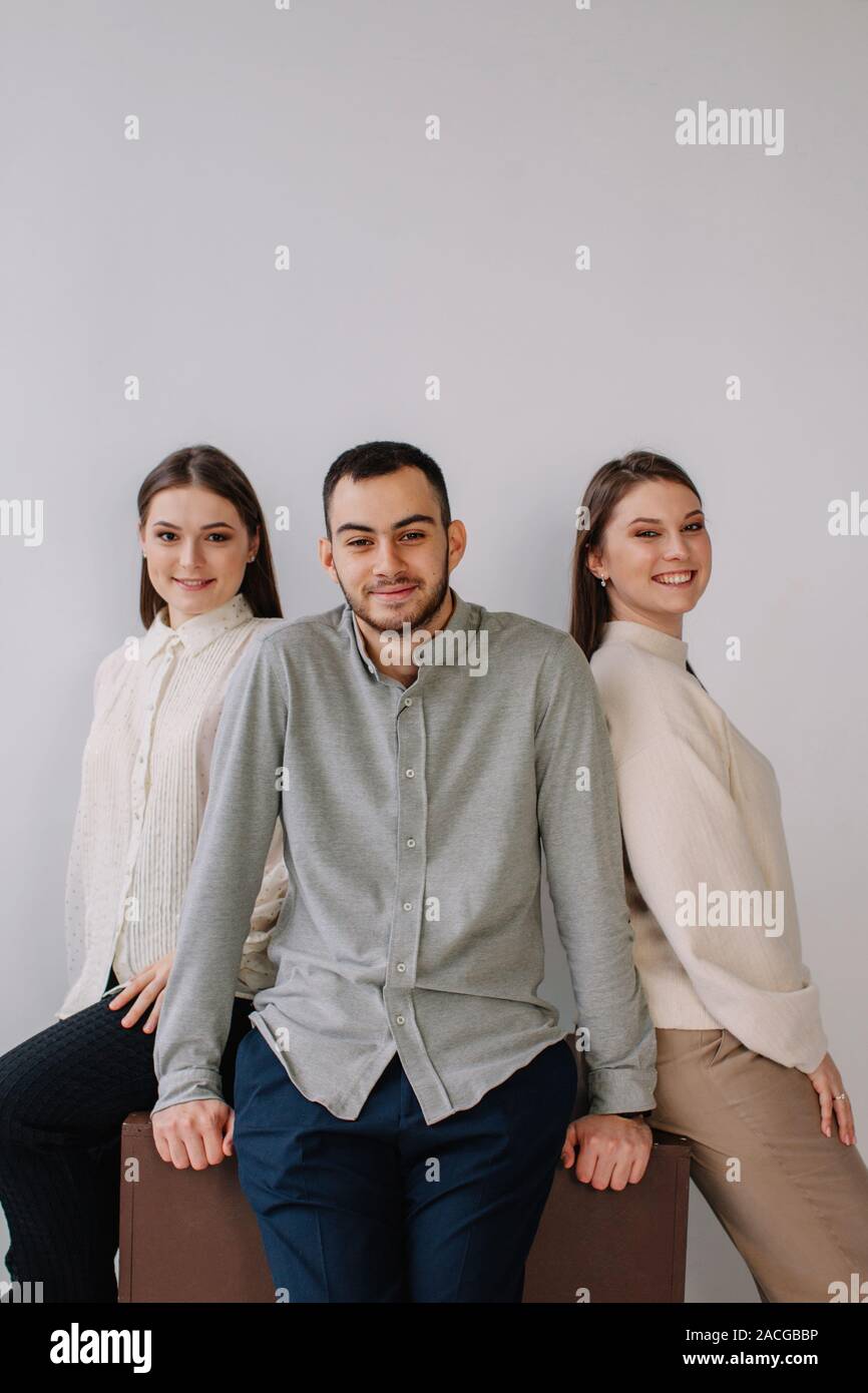 Portrait of three people sitting on the edge of a table Stock Photo