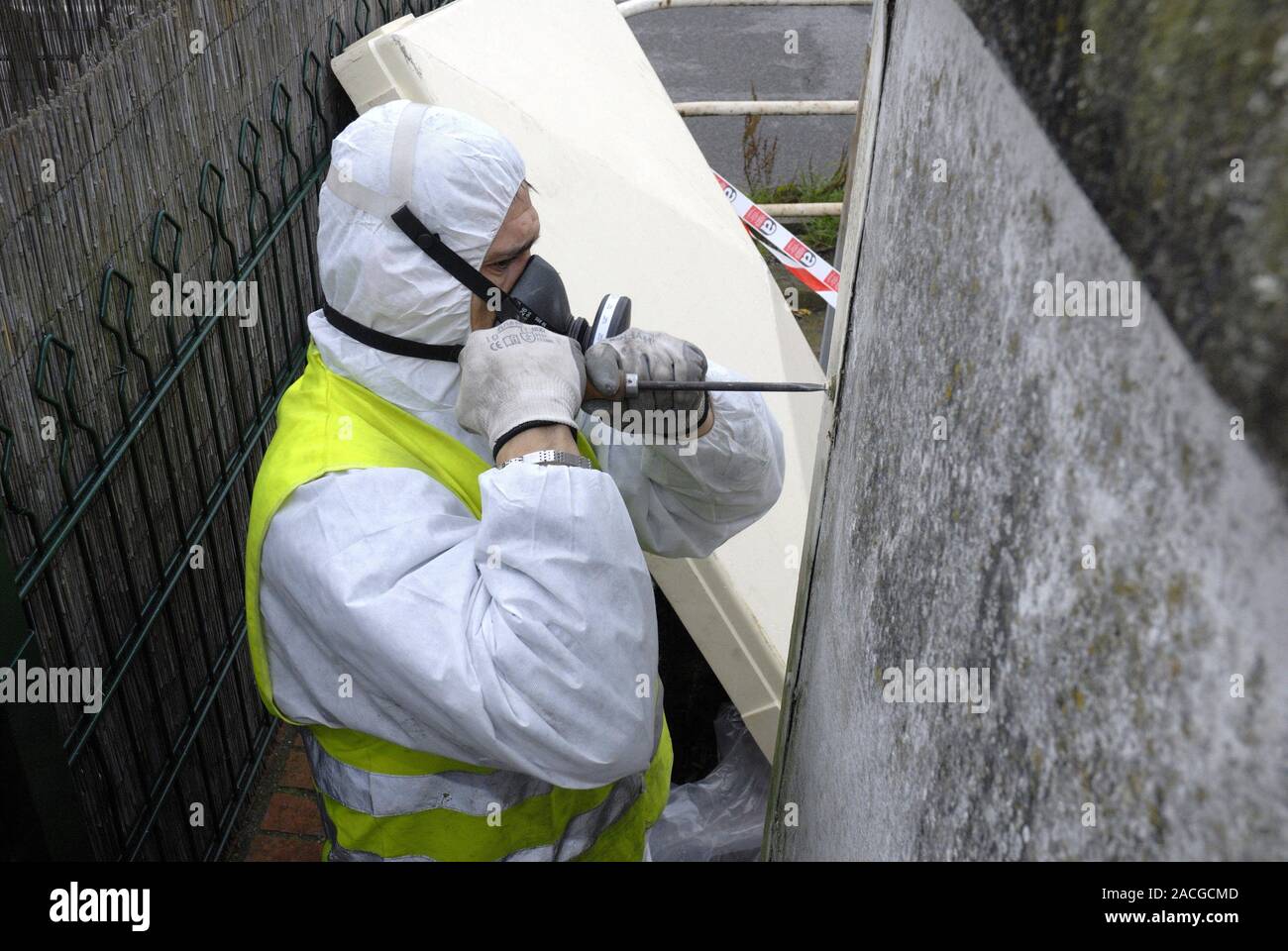 Asbestos removal. Worker in protective clothing dismantling a hut 