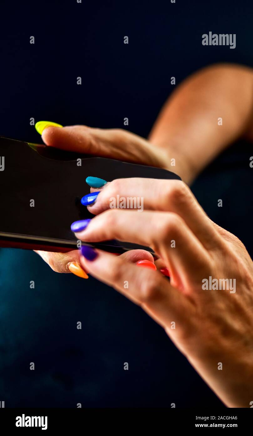 A woman holding a mobile phone with multi-color fingernails. Stock Photo