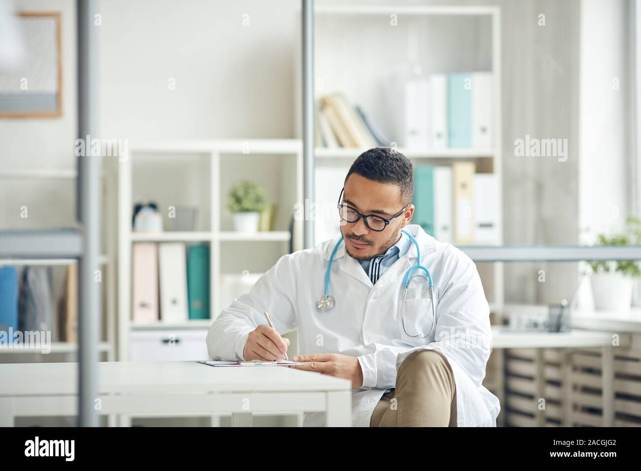 Portrait of African-American doctor filing in papers while sitting at desk in clinic, copy space Stock Photo