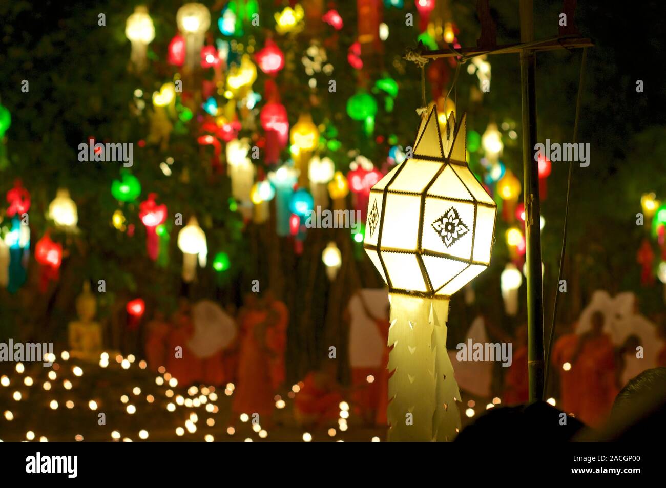 Traditional Thai paper lantern with monks in the blurred background and other colorful lanterns hanging on a tree captured at the Wat Phan Tao Stock Photo
