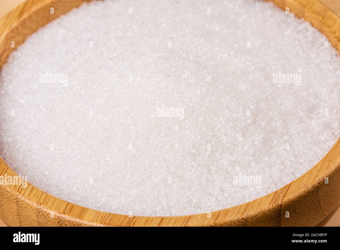 Wooden bowl full of granulated sugar on a wooden background Stock Photo