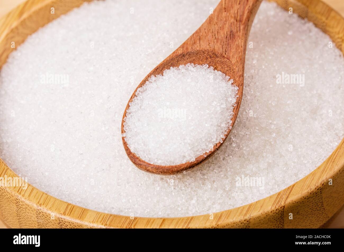 Wooden bowl full of granulated sugar with a wooden spoon on a wooden background Stock Photo