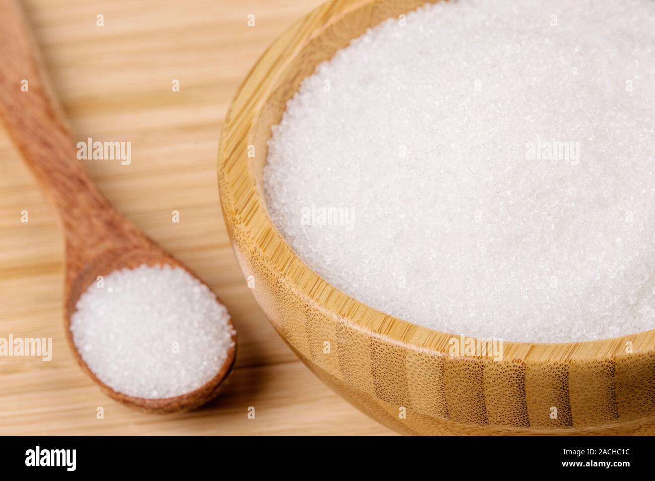 Wooden bowl full of granulated sugar with a wooden spoon on a wooden background Stock Photo