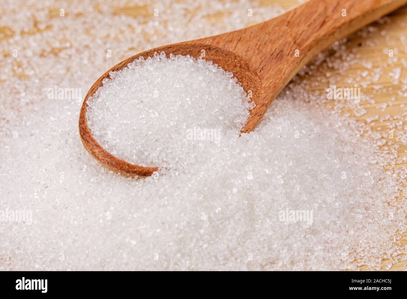 Wooden spoon full of sweet granulated sugar on a wooden background Stock Photo