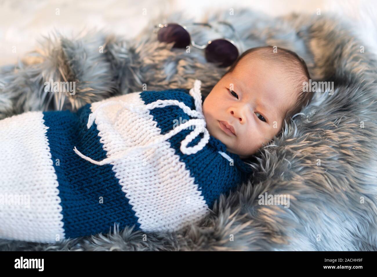 newborn baby boy swaddled in a knit wrap on a fur bed Stock Photo