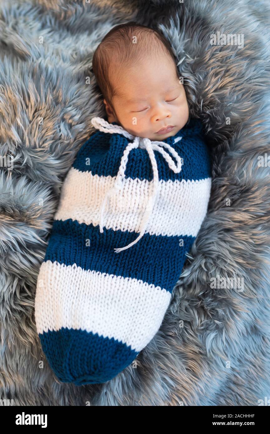 newborn baby boy sleeping and swaddled in a knit wrap on a bed
