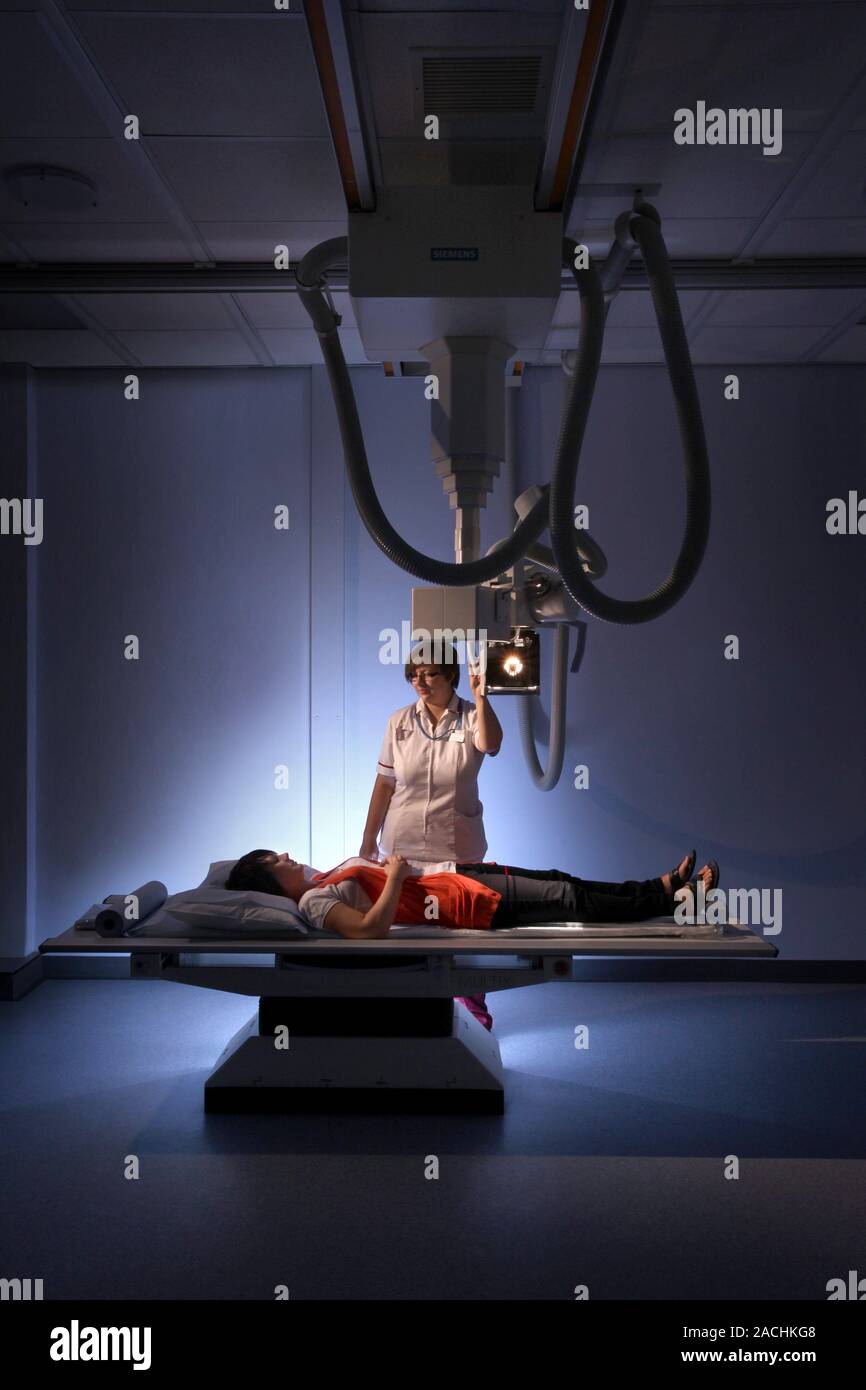 Taking an X-ray. Radiographer (standing) taking an X-ray of a female ...