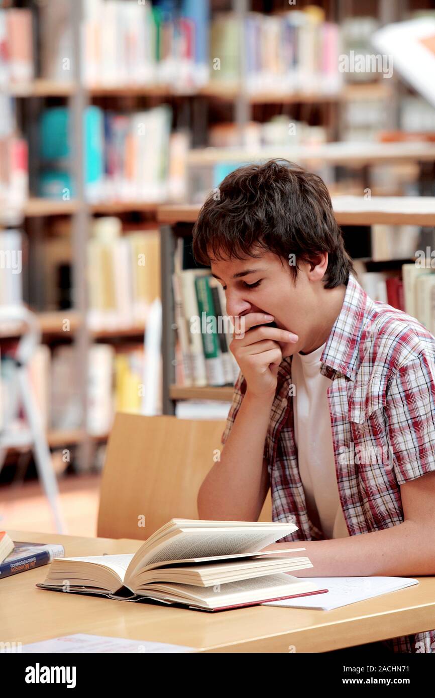 Library. Young man yawning whilst trying to study in a library. Stock Photo