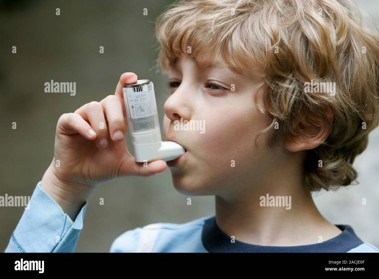 Asthma inhaler use. Boy using an inhaler to treat his asthma. The inhaler contains