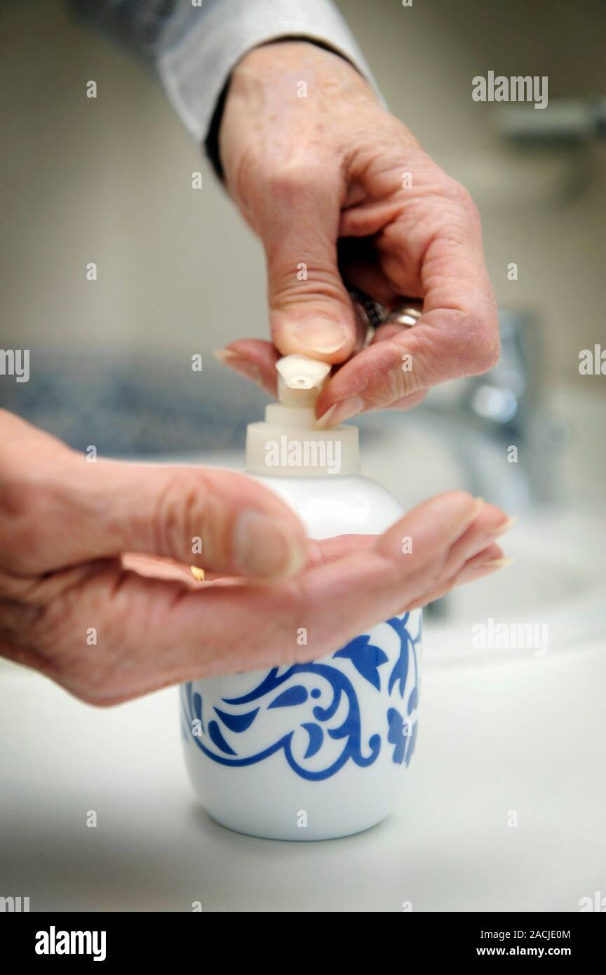 Using a soap dispenser. Elderly lady dispensing liquid soap onto her