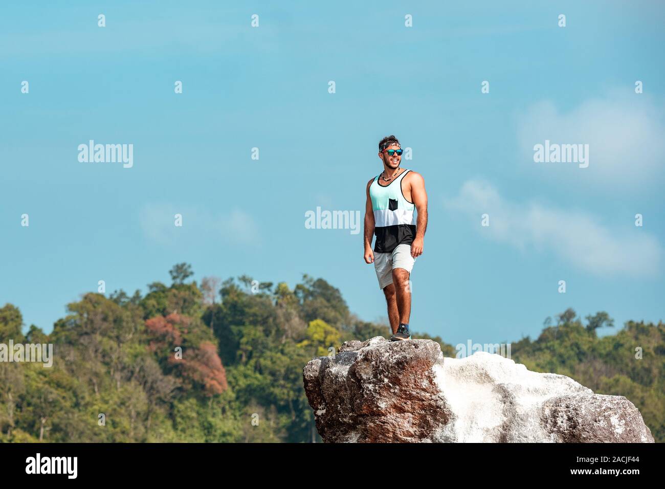 Sporty strong man is standing on big rock at mountain top against blue sky and forest Stock Photo