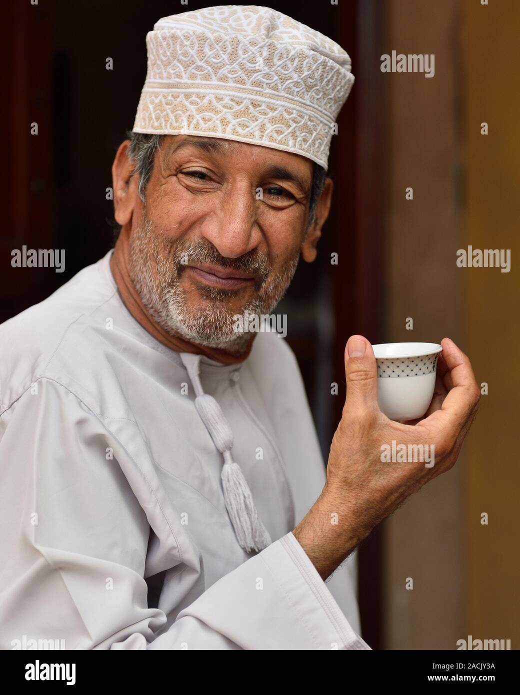 Muscat, Oman, NOVEMBER 24rd, 2018: portrait of an older man, dressed in the traditional  omani dress, with the small cup of the coffee. Stock Photo