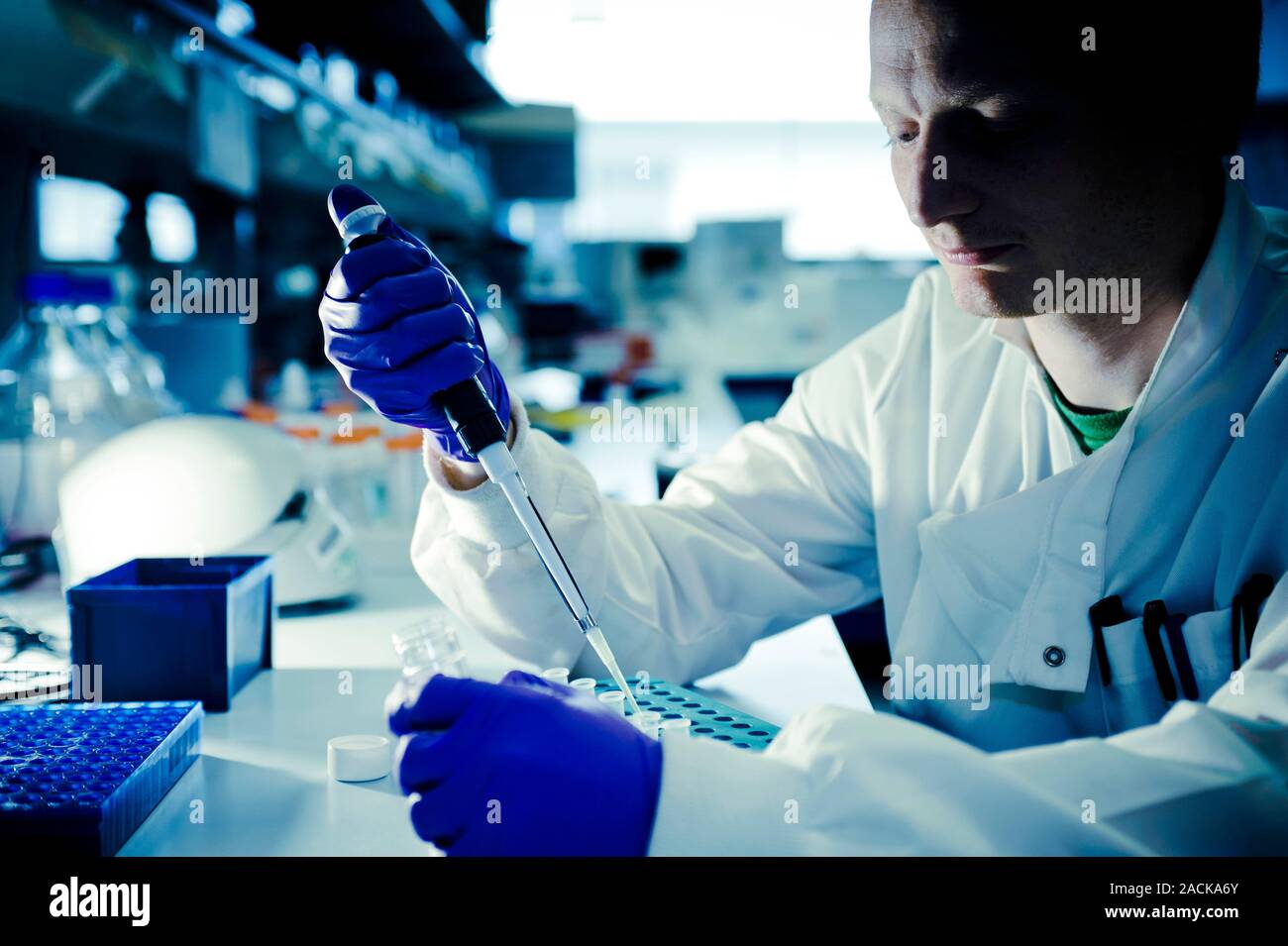 Technician using a pipette to transfer a liquid sample into a small ...